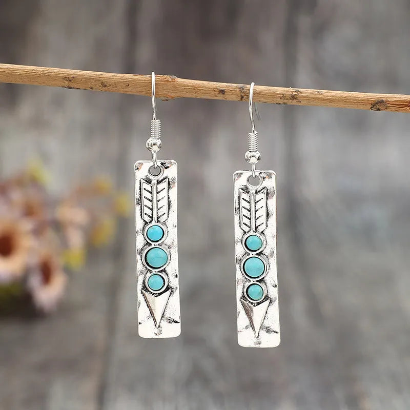 Silver geometric drop earrings with turquoise inlaid accents on a plain background