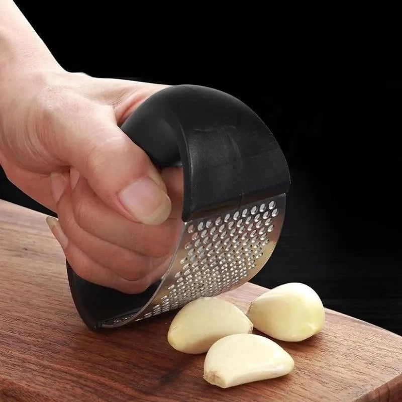 Stainless steel manual garlic press with coloured non-slip handle on a kitchen counter.