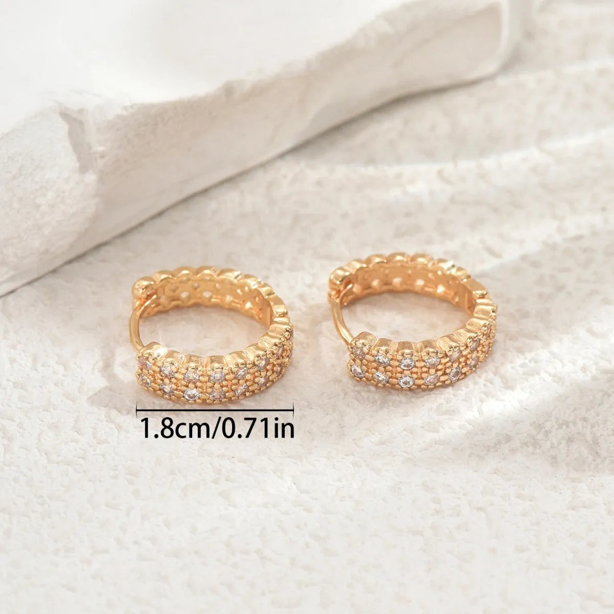 A pair of copper geometric ear studs featuring a round ring with a central dot, on a grey background.