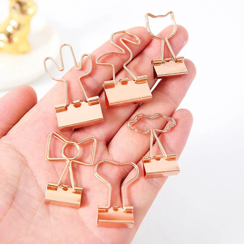 Small gold-plated metal office clip with a long tail, shown in decorative flamingo, love, cat, cactus, and bow shapes.
