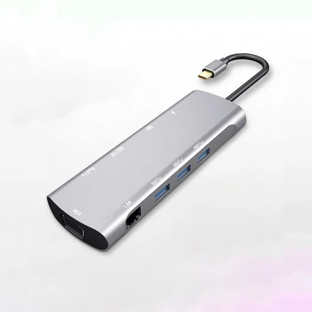 Grey aluminium USB-C docking station with HDMI, VGA, USB 3.0, and PD charge ports on a wooden desk.
