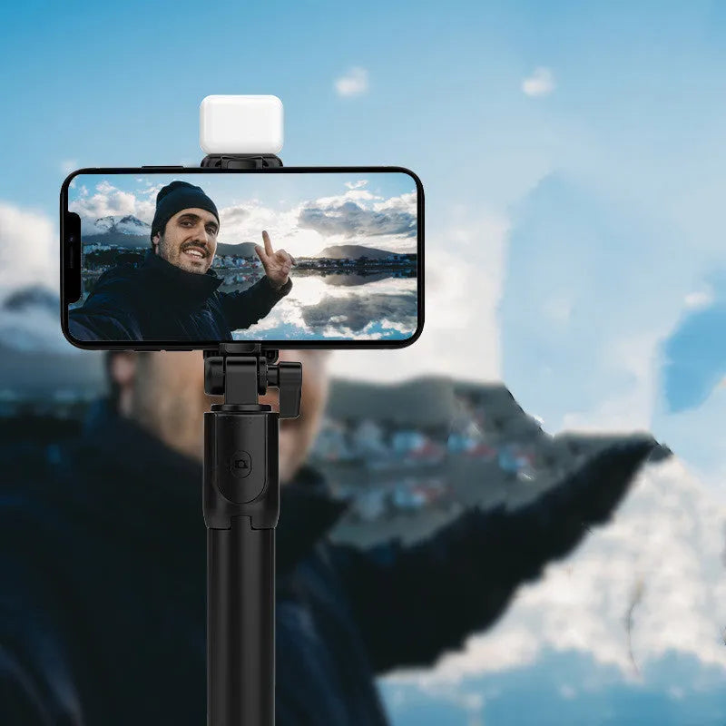 Black aluminium Bluetooth selfie stick with extended tripod legs and a phone mounted in the 360-degree rotating holder.