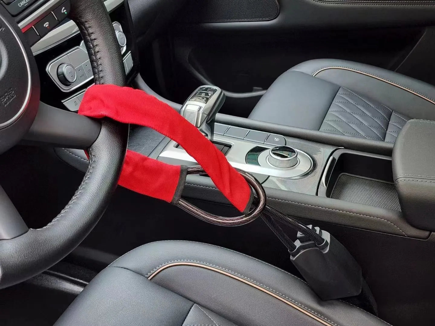 Red car steering wheel lock with iron cable secured around a steering wheel.