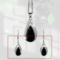Black and red teardrop-shaped glass pendant necklace and matching stud earrings set on a grey background.