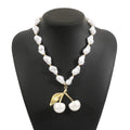 Gold irregular cherry fruit and pearl necklace on adjustable chain against white background.