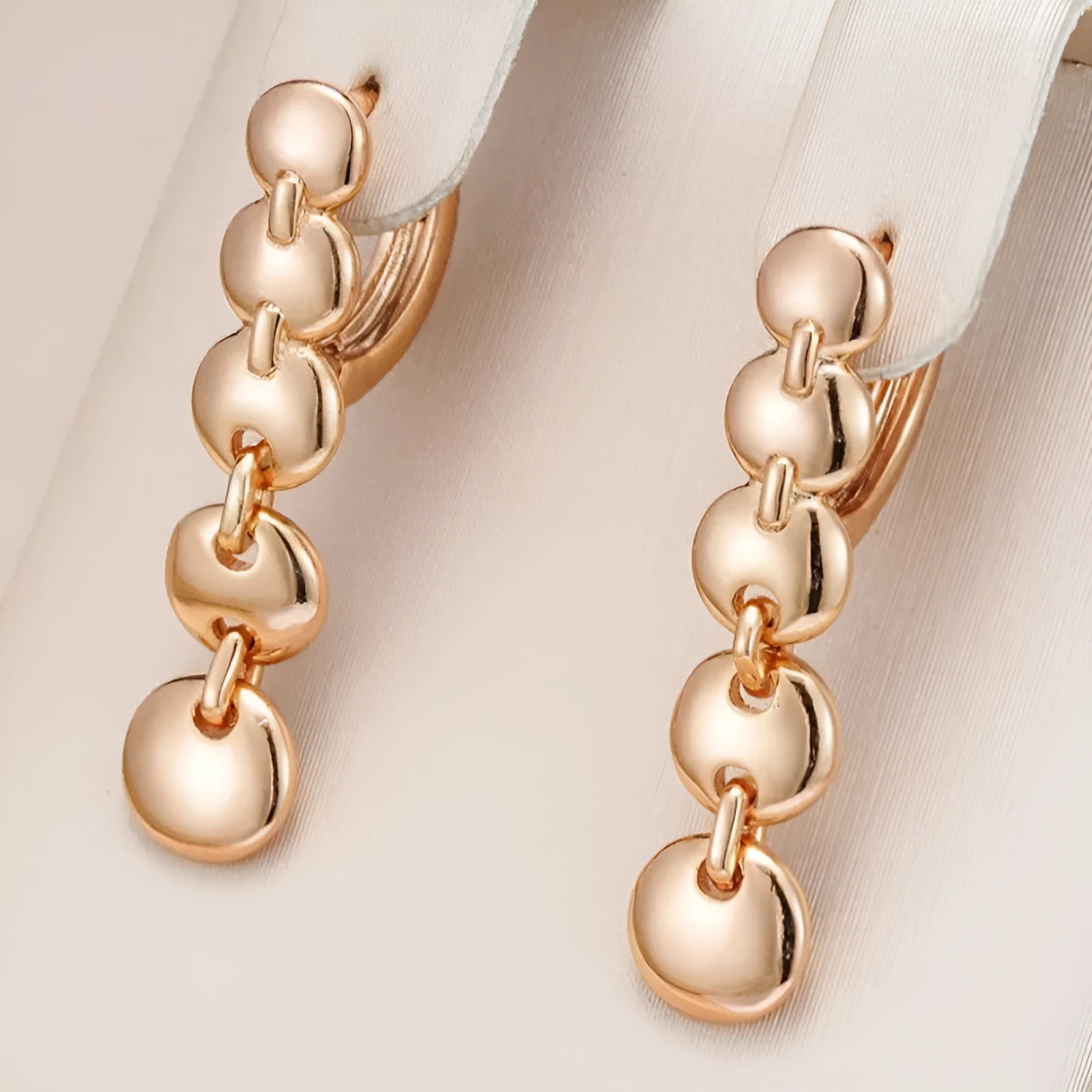 A pair of long, round, woven copper earrings with a gold finish, showing textured detail.