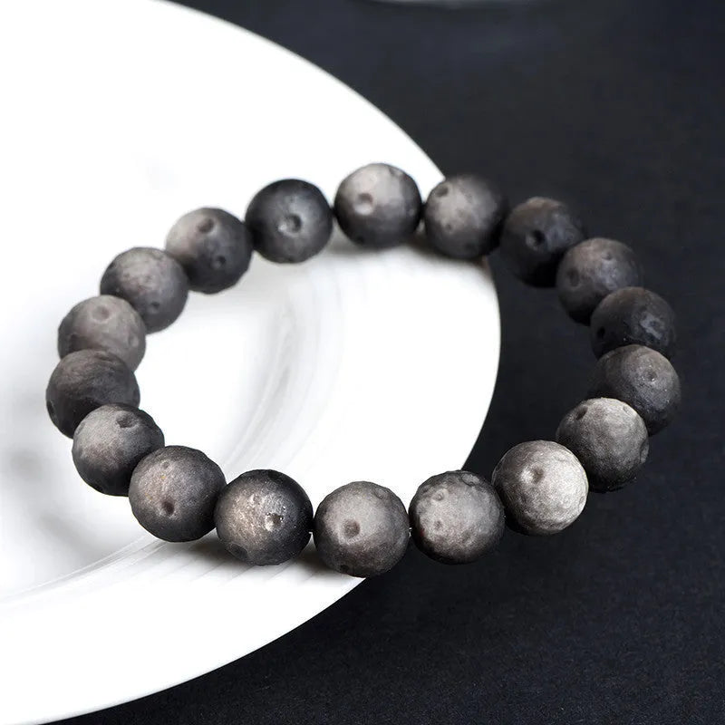 A natural obsidian crater ball bracelet in gold or silver meteorite colour on a wrist, showing textured bead detail.