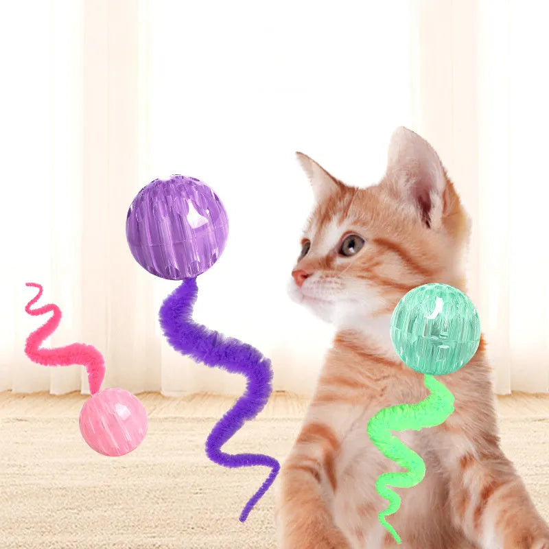 Green bouncy worm-shaped cat toy with a long plush tail on a wooden floor.