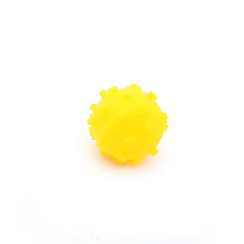 Bright blue, green, pink and yellow spiked squeaky dog balls for small breeds on a grass background.