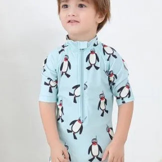 Toddler boy wearing a penguin print long sleeve one-piece swimsuit and matching swimming cap.