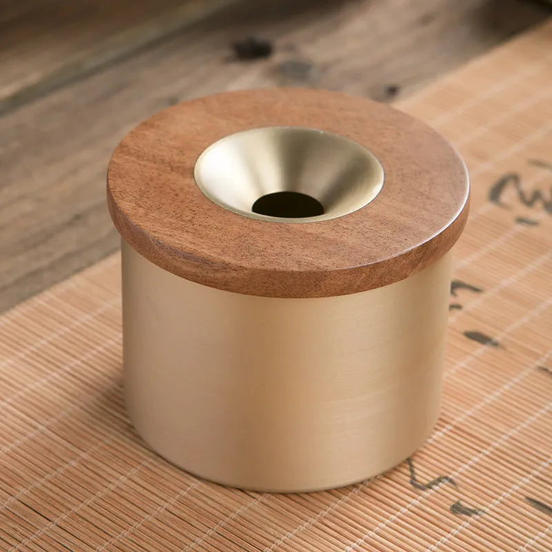 Brass-coloured copper ashtray with a wooden lid on a tabletop.