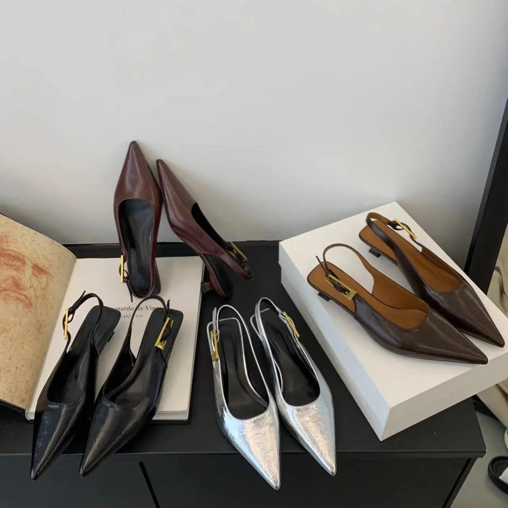 Women's black pointed toe leather strap shoes with a low rubber heel shown from the side.