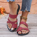 A pair of casual black beach slippers with a one-line design and hollow out details on a sandy background.
