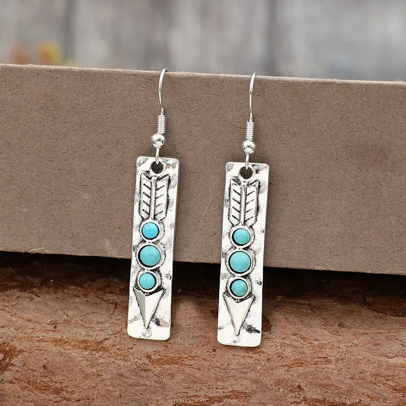 Silver geometric drop earrings with turquoise inlaid accents on a plain background