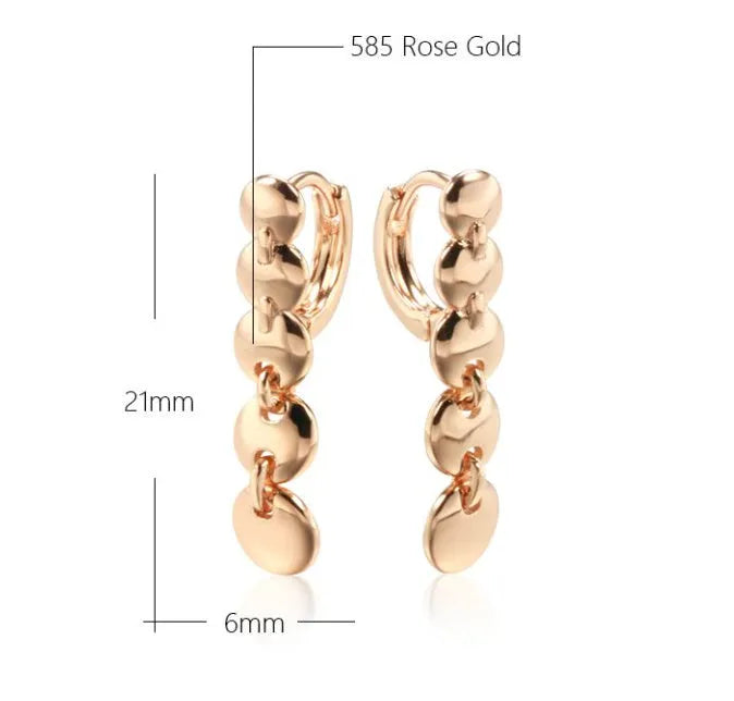 A pair of long, round, woven copper earrings with a gold finish, showing textured detail.