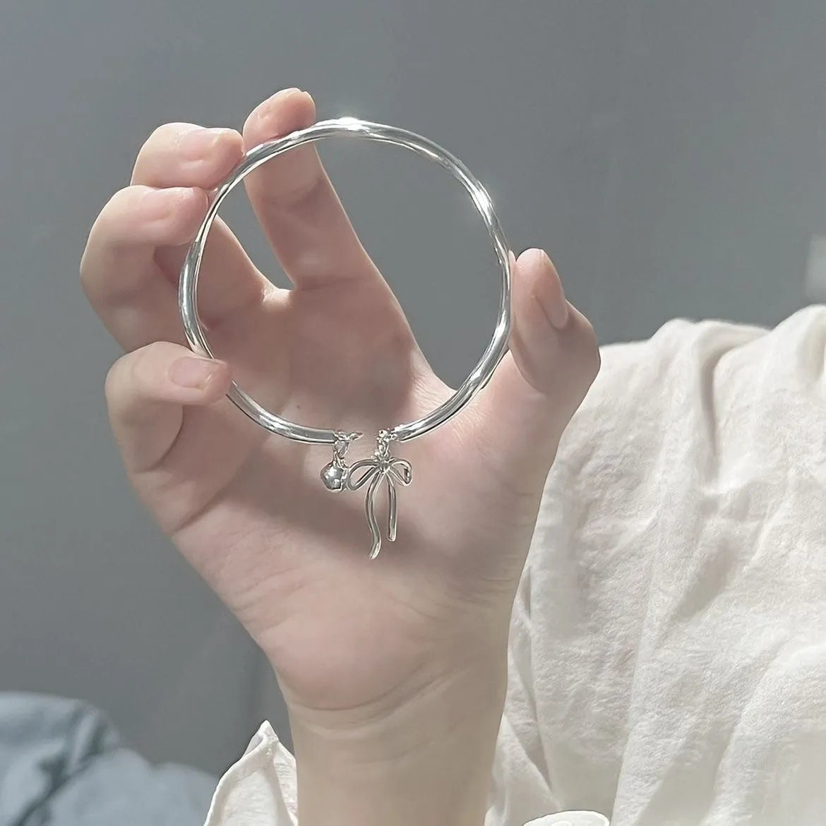 Silver-toned adjustable bracelet with a detailed bow charm on the wrist, showing the opening clasp mechanism.