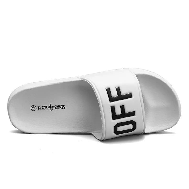 Large black and white open-toe men's slippers with rubber soles, shown on a wooden floor.