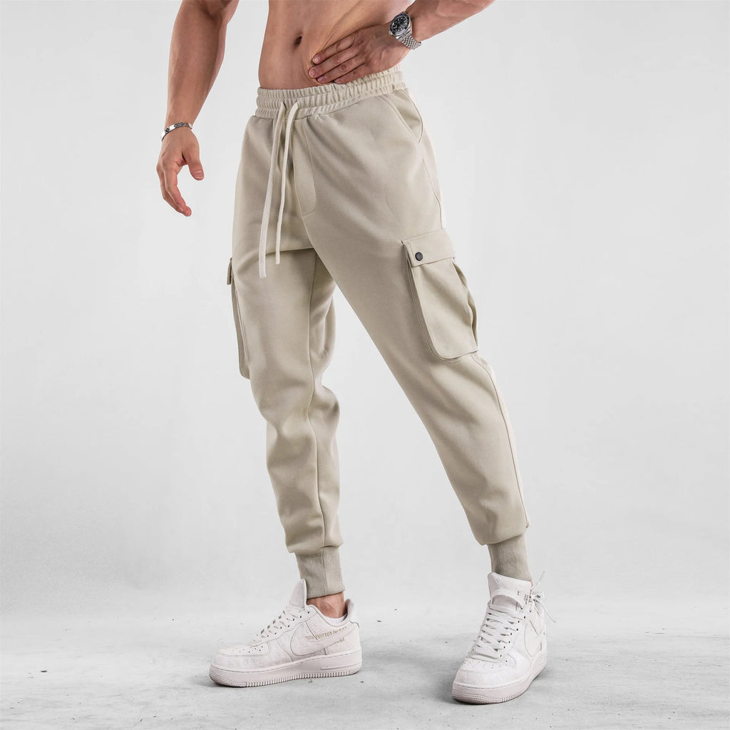 Men's loose-fit beige cotton trousers with tied ankle cuffs and multiple pockets on the legs.