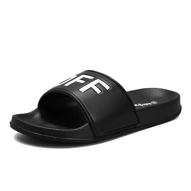Large black and white open-toe men's slippers with rubber soles, shown on a wooden floor.