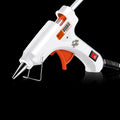 White electric hot glue gun with a metal stand and anti-heat blanket on a table.
