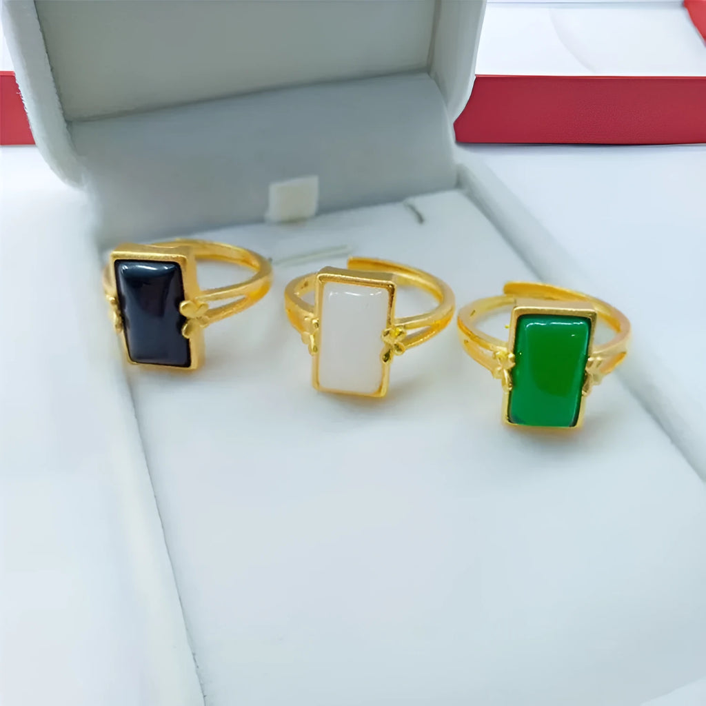 Adjustable brass gold-plated ring with a coloured gemstone inlay on a finger.