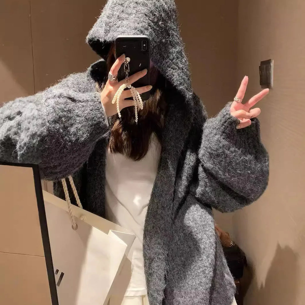 A woman wearing a thick, dark grey hooded cardigan with a loose, longline fit.