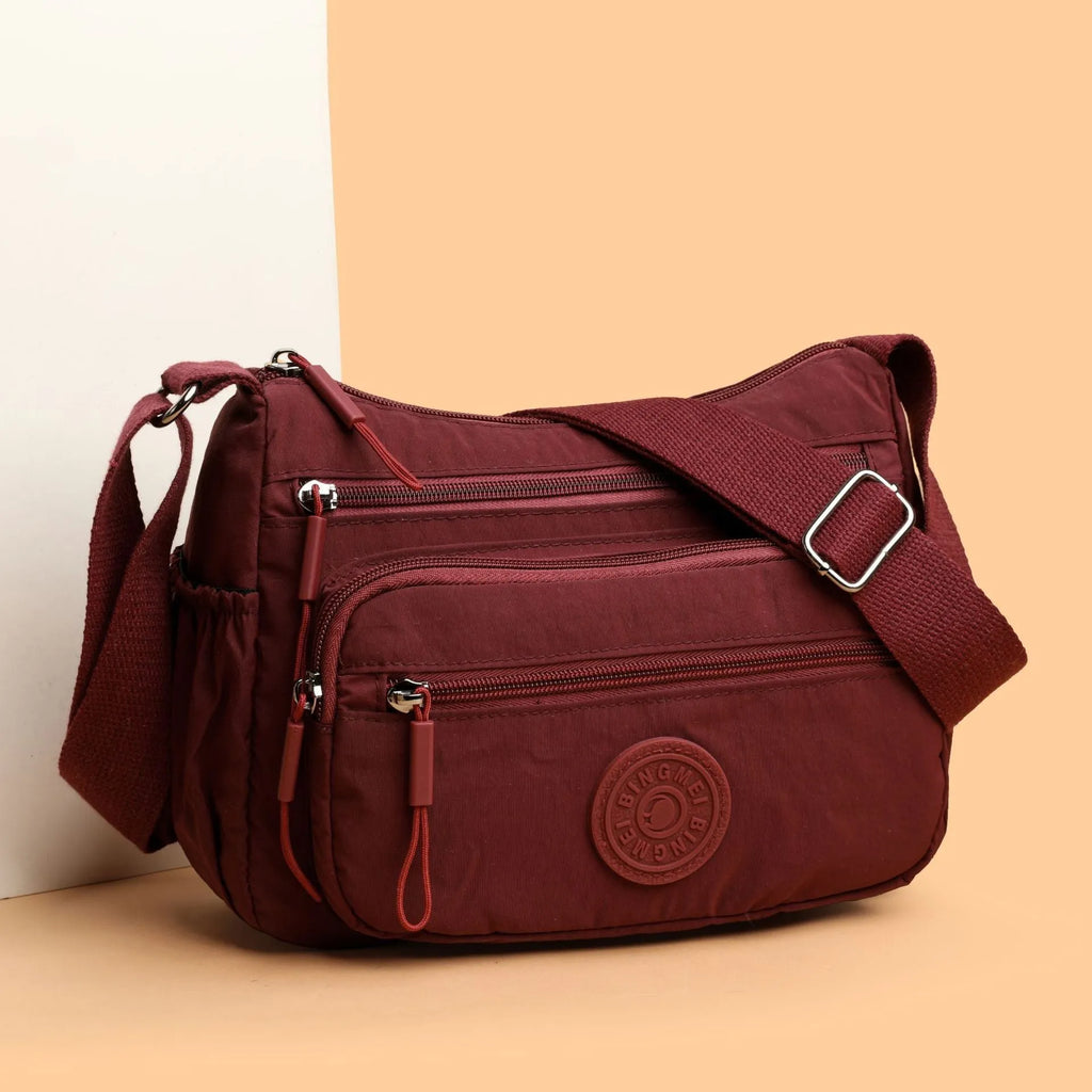 Soft water-repellent nylon crossbody bag with a three-dimensional front pocket and adjustable strap.