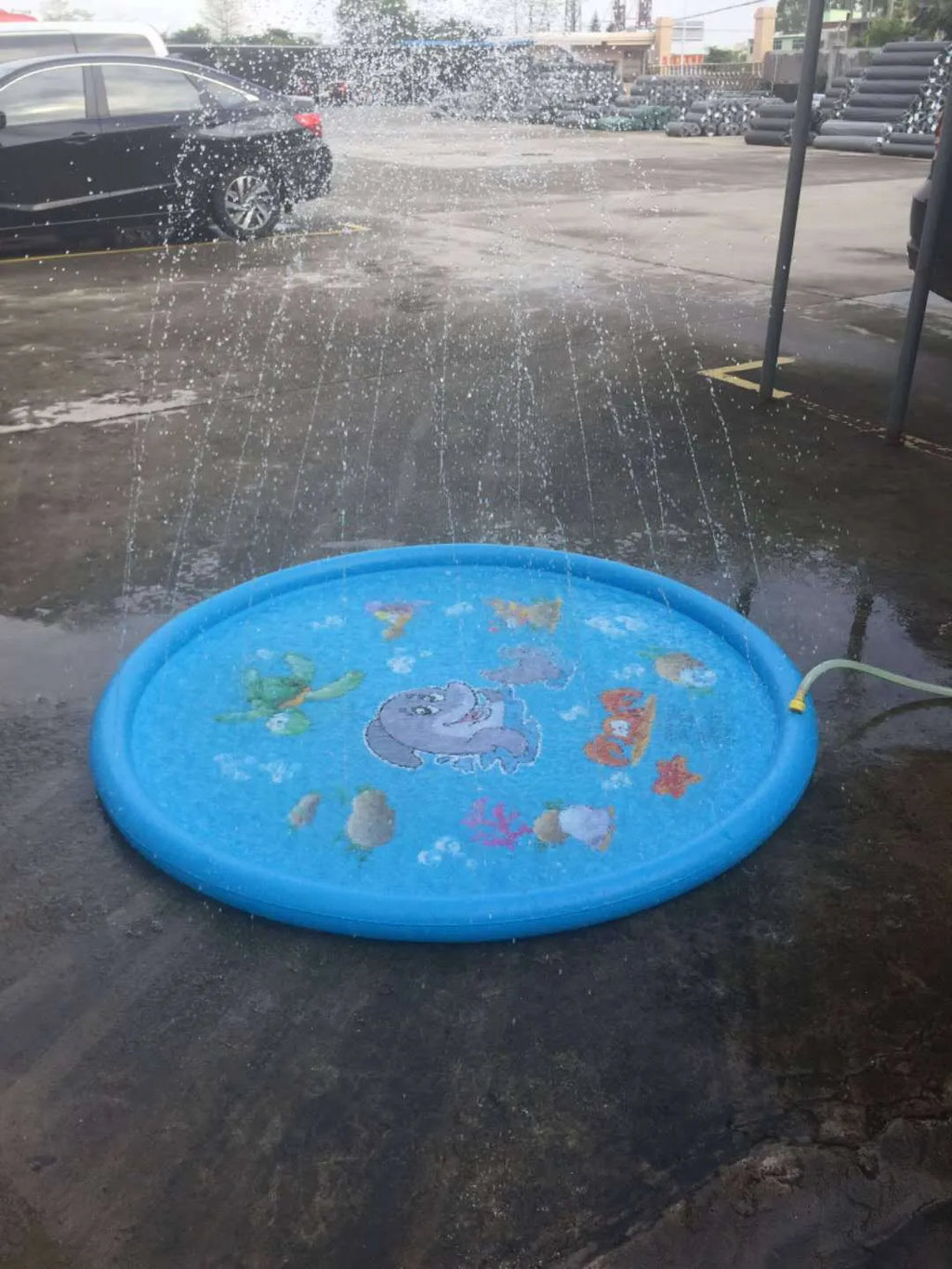 Blue children's water spray mat with marine animals laid on grass, connected to a garden hose.