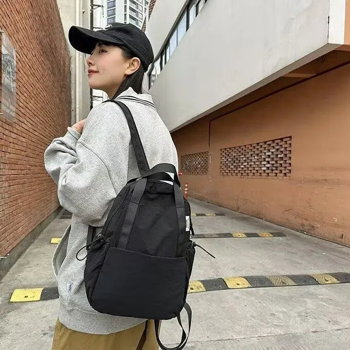 Simple solid colour nylon backpack with a curved shoulder strap and lock closure, shown in black.