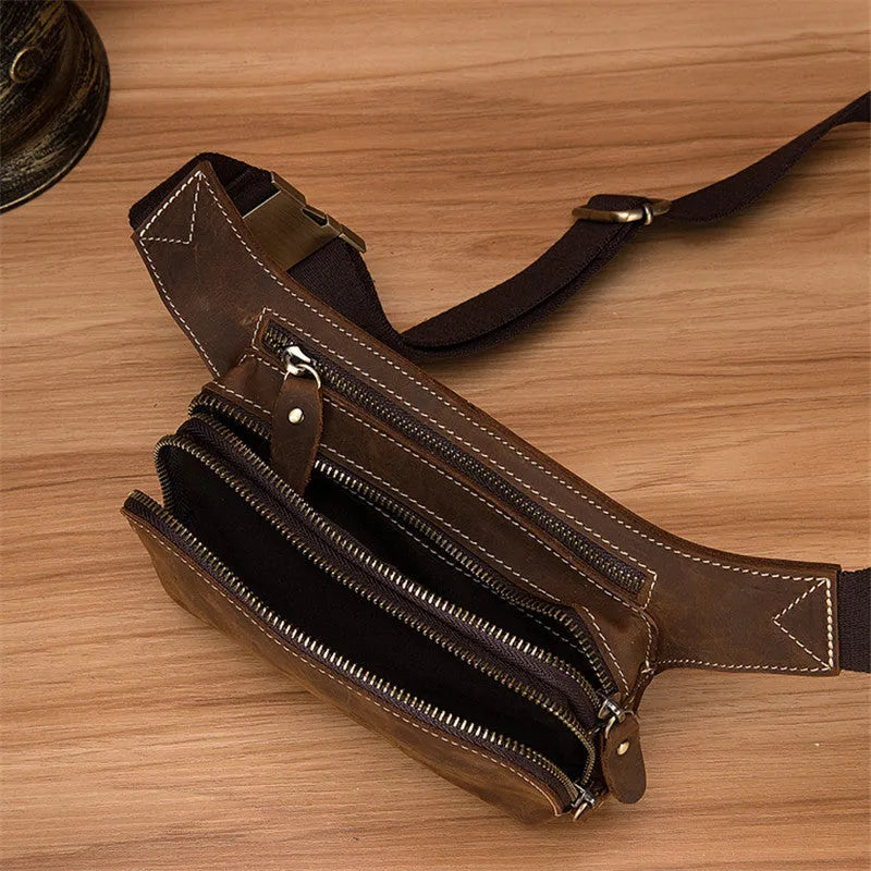 Brown top-layer cowhide men's sports waist bag shown with a 10-inch laptop and phone next to it for scale.
