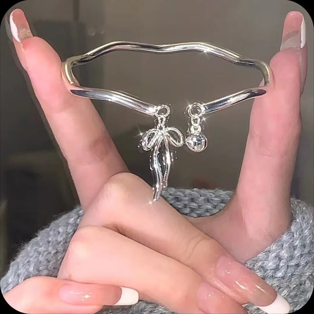 Silver-toned adjustable bracelet with a detailed bow charm on the wrist, showing the opening clasp mechanism.
