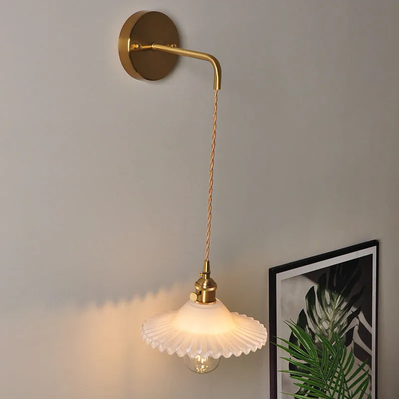 Brass wall lamp with an adjustable smoked grey glass lotus shade mounted beside a bed.