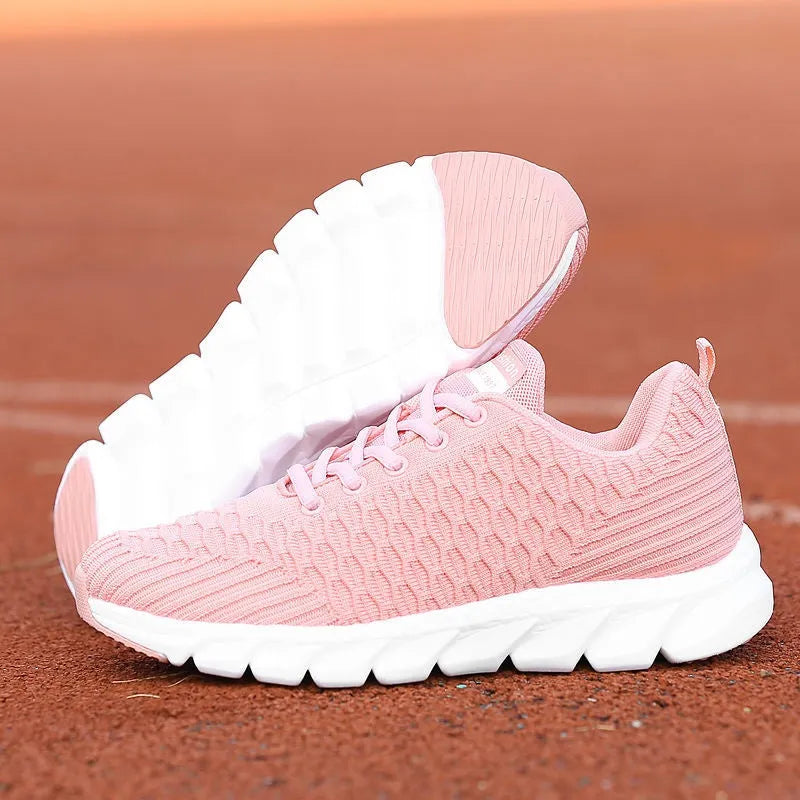 Women's running shoes in black, pink, and white colours showing fly weaving upper and rubber outsole.