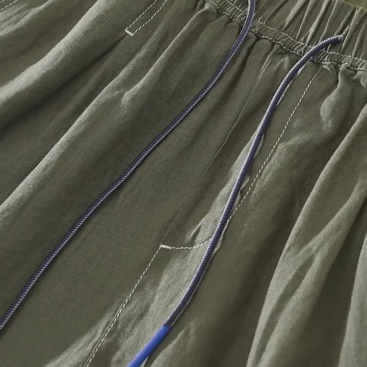 Men's loose fit linen shorts in green, showing straight drooping leg and drawstring waist.
