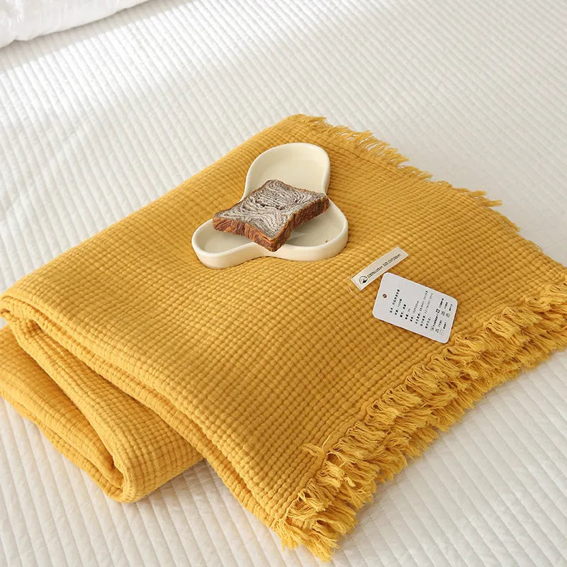 Four-layer gauze cotton blanket with tassel edging in avocado green, laid flat.