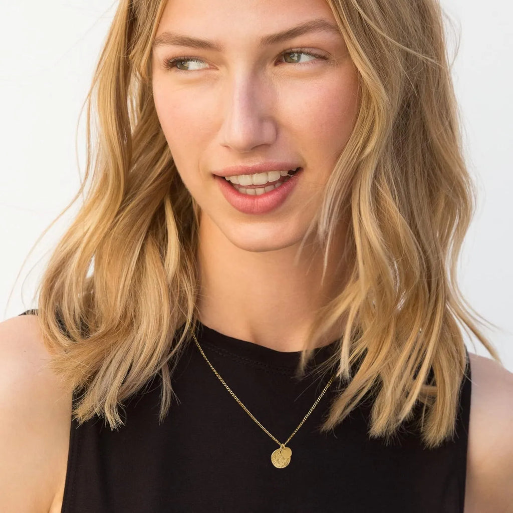 Round coin stainless steel pendant necklace in gold with adjustable side chain on a white background