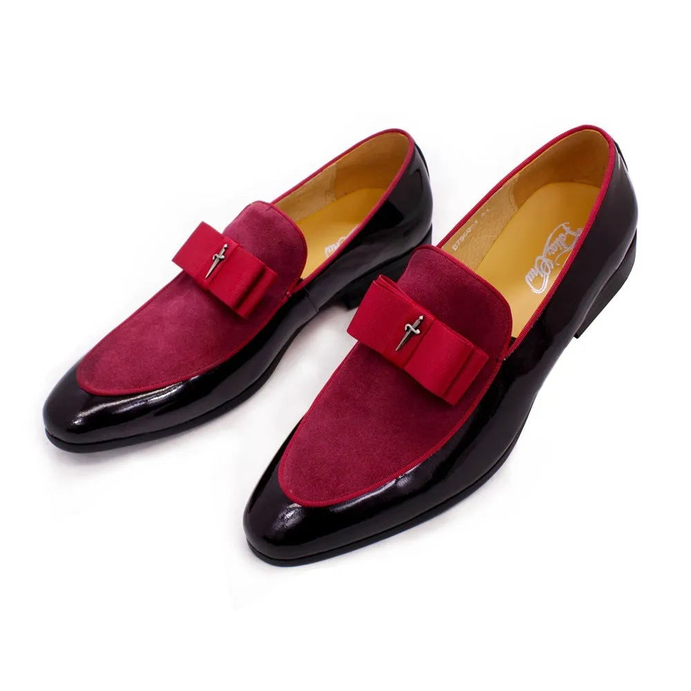 Men's black tassel loafers with glossy patent leather upper and matte leather toe holder on a wooden floor.