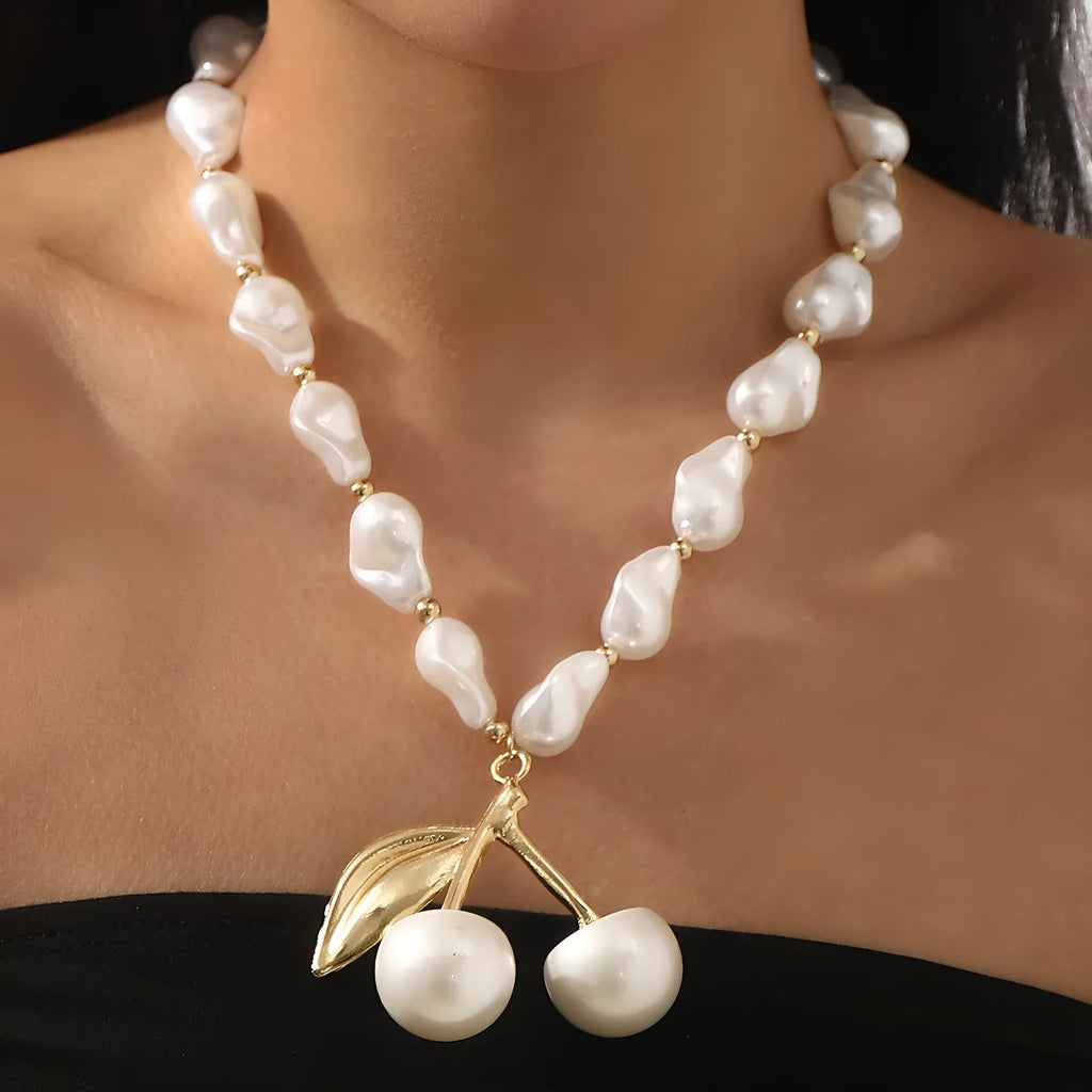 Gold irregular cherry fruit and pearl necklace on adjustable chain against white background.