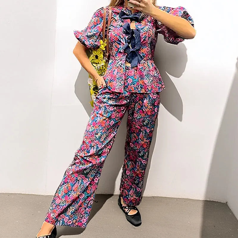 Women's floral printed trousers suit with a tie-neck blouse featuring puff sleeves and matching trousers.