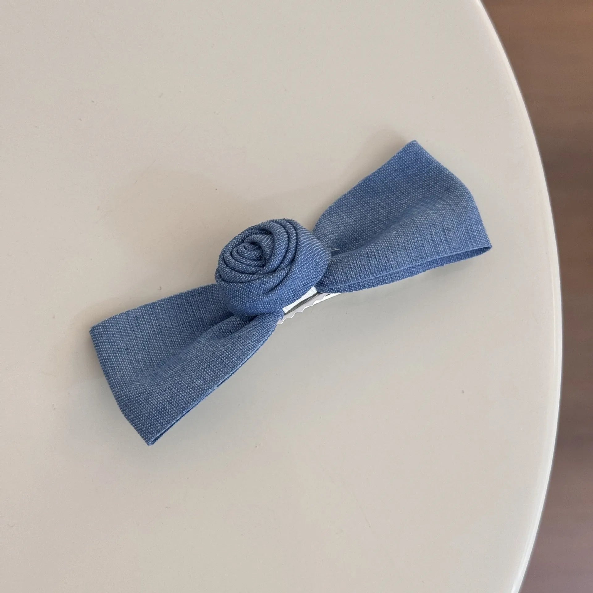 A women's hair clip barrette with a soft blue cloth bow and lace decoration on a plastic clip.