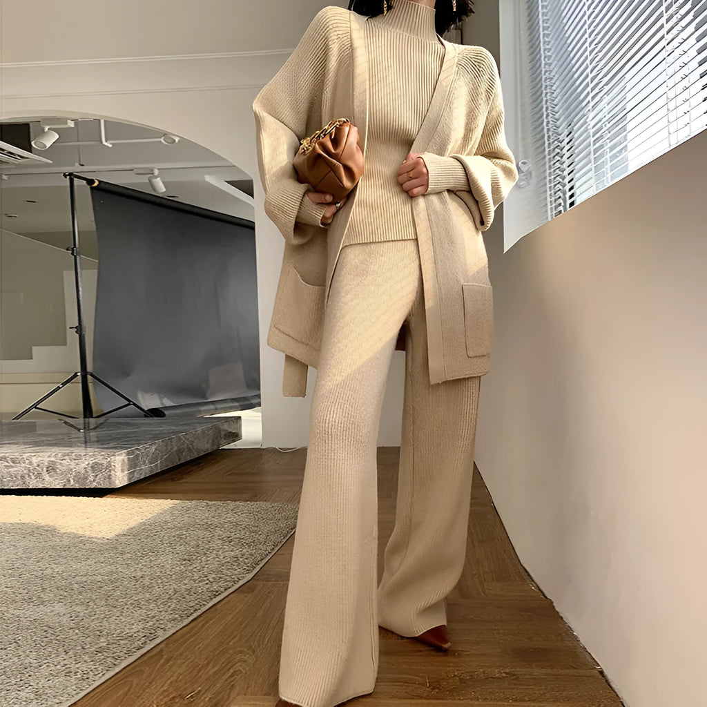 Women's apricot knitted three-piece set showing V-neck top, wide-leg trousers, and longline cardigan with leather stitching detail.