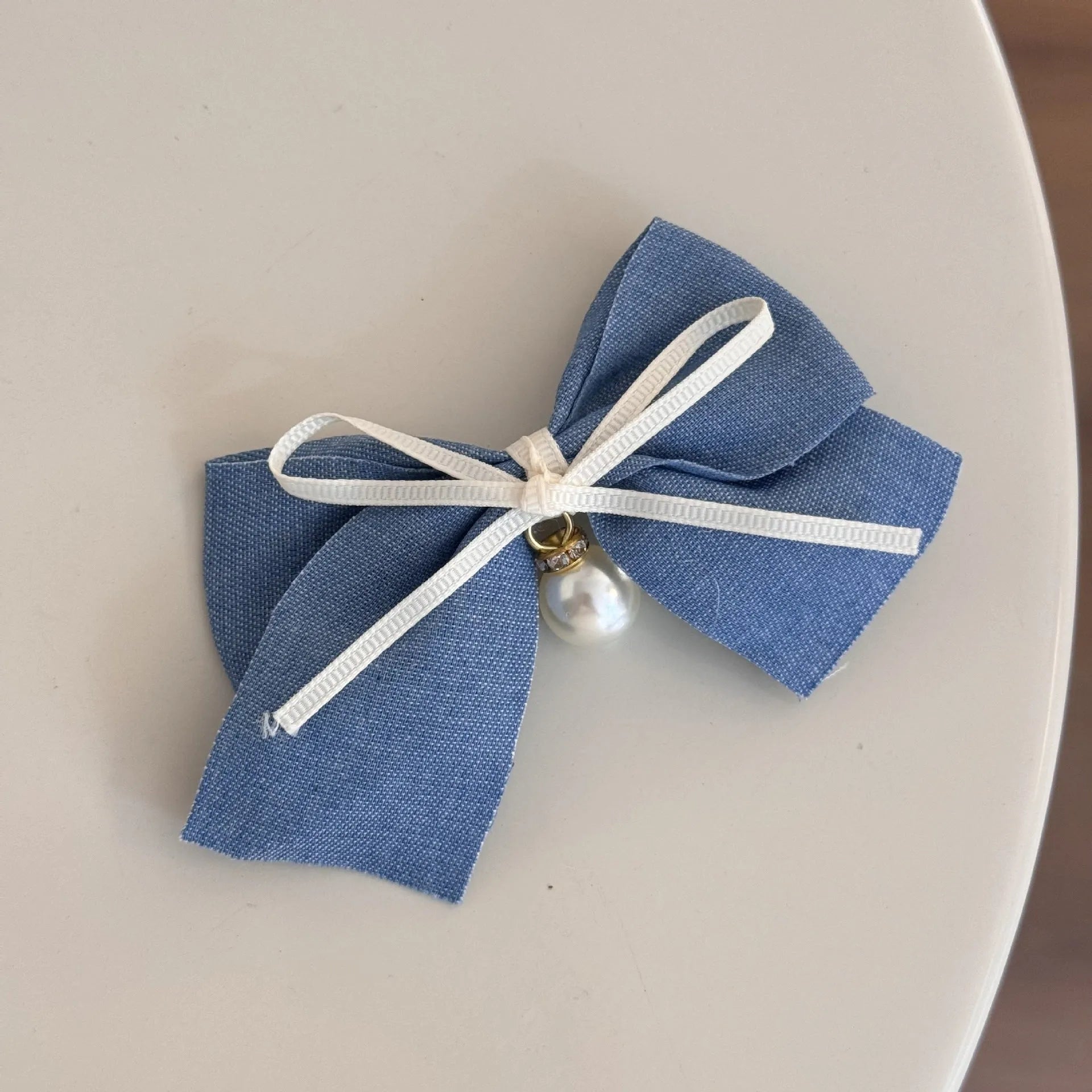 A women's hair clip barrette with a soft blue cloth bow and lace decoration on a plastic clip.