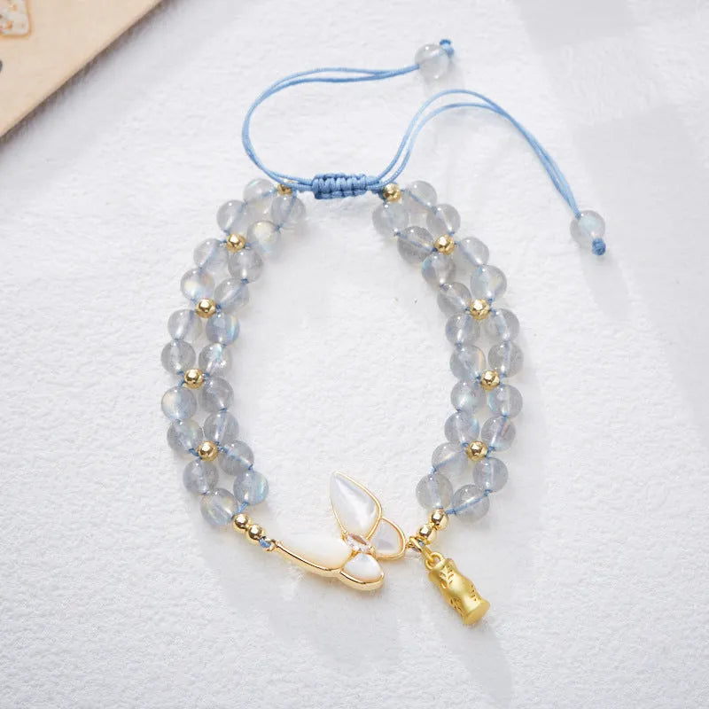 Close-up of a women's woven bracelet with a butterfly motif and a central aquamarine gemstone bead.
