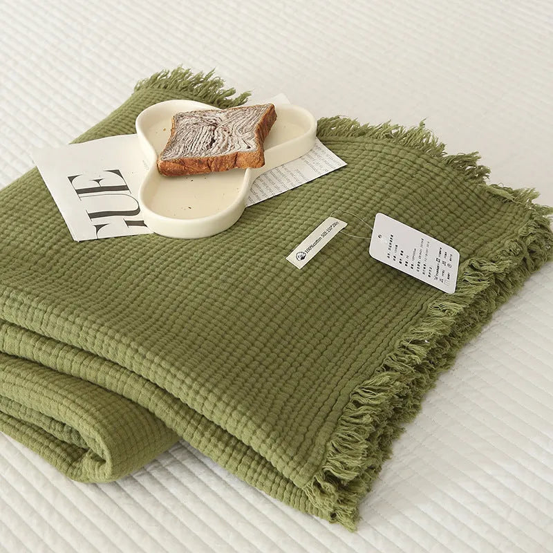 Four-layer gauze cotton blanket with tassel trim in avocado green, laid flat.