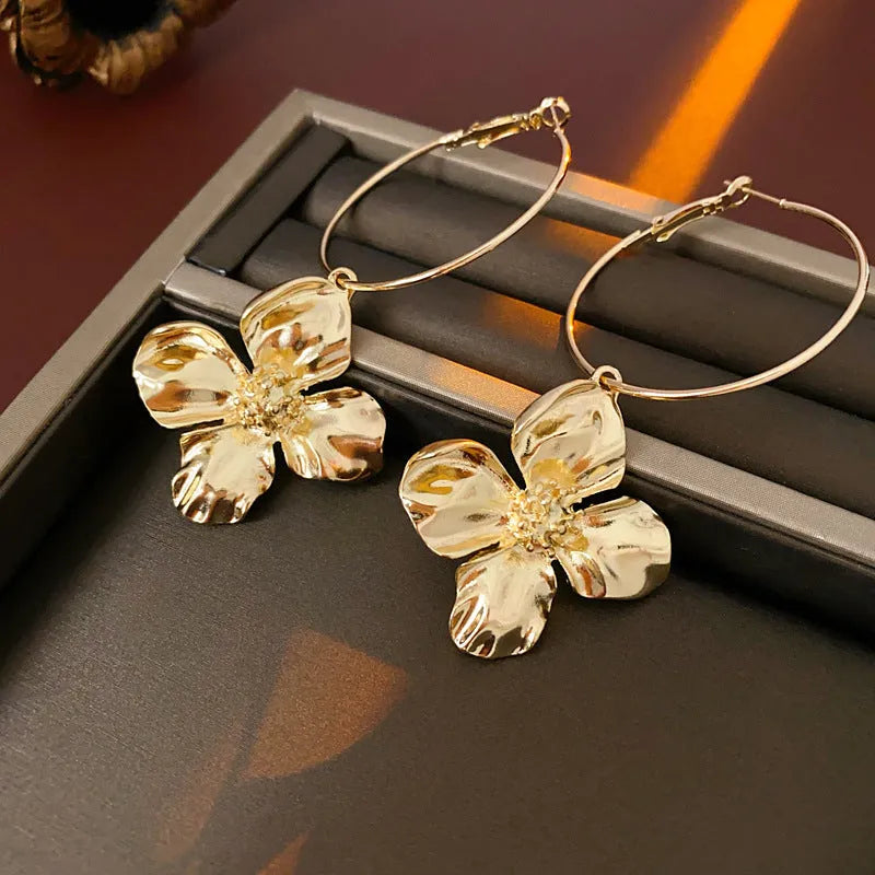 A pair of geometric flower-shaped metal earrings with a silver needle detail, shown in gold and silver electroplated finishes.