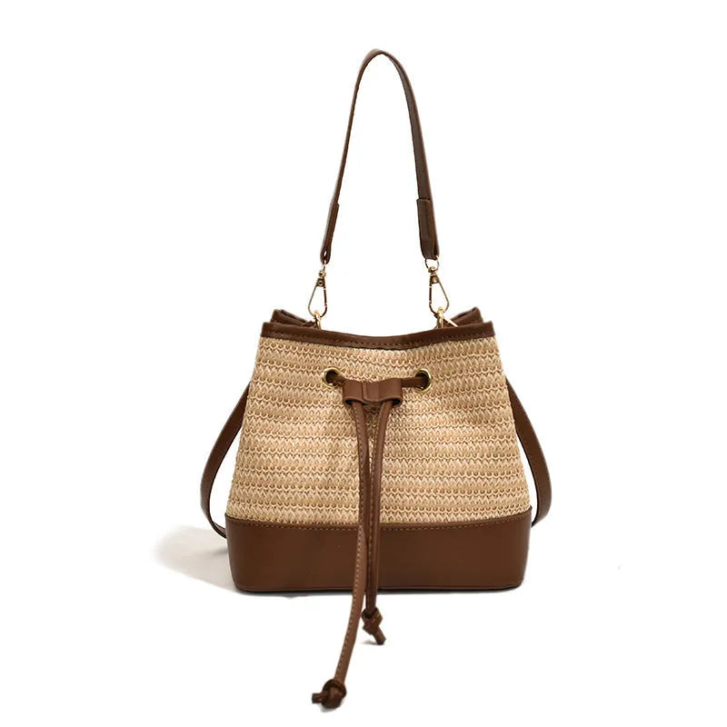 Brown woven straw women's crossbody bucket bag with adjustable strap on a table.