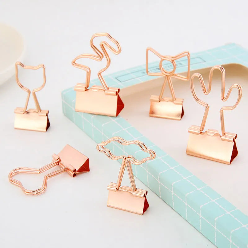 Small gold-plated metal office clip with a long tail, shown in decorative flamingo, love, cat, cactus, and bow shapes.