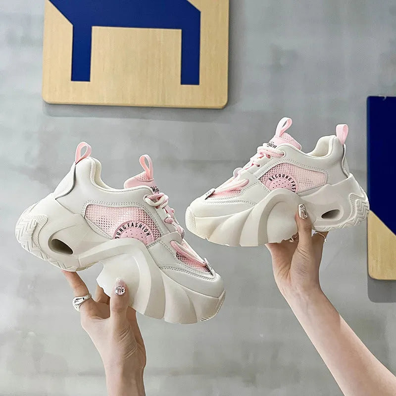 Women's pink sneakers with a cross strap and thick sole on a neutral background.