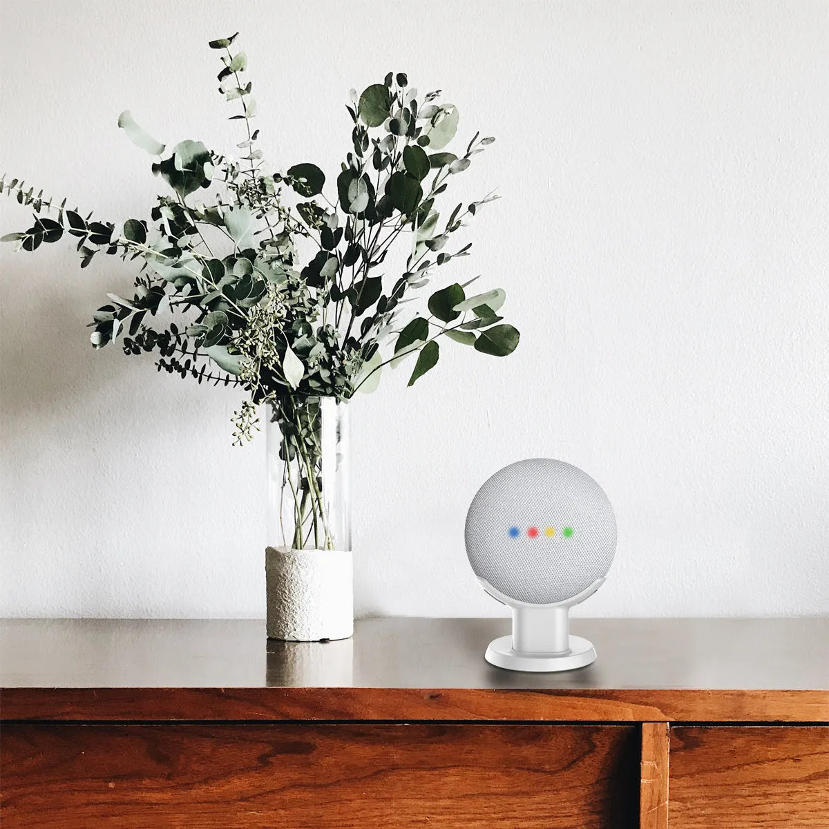 Black or white plastic stand holding a Google Home Mini voice assistant on a desk.