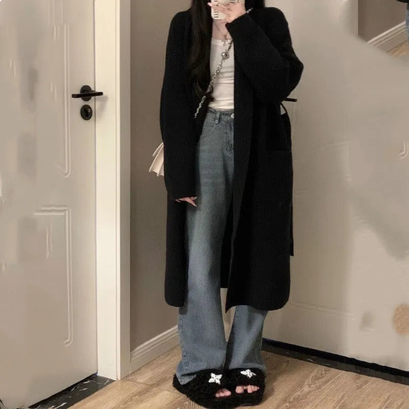 A woman wearing a loose, thick knitted chenille cardigan in a solid colour, showcasing its long sleeves and medium length.